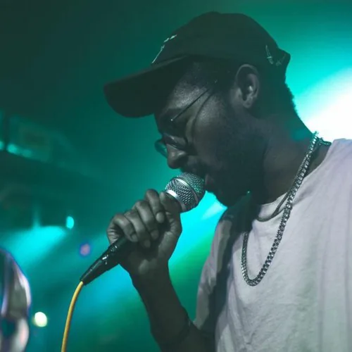 Lil Gohan performing into a microphone under teal stage lights.